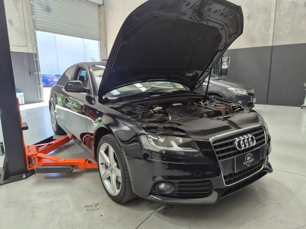 Black Audi vehicle with hood raised, positioned on a lift in a modern garage