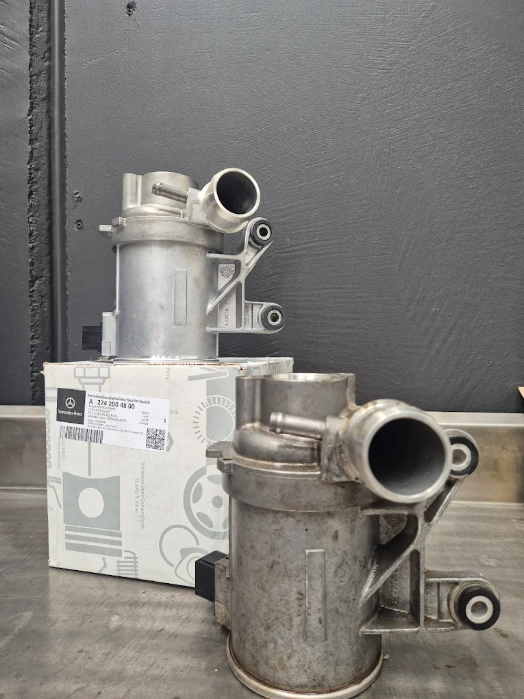 Mercedes-Benz engine components displayed on a workbench, featuring a new part in its packaging and a used part