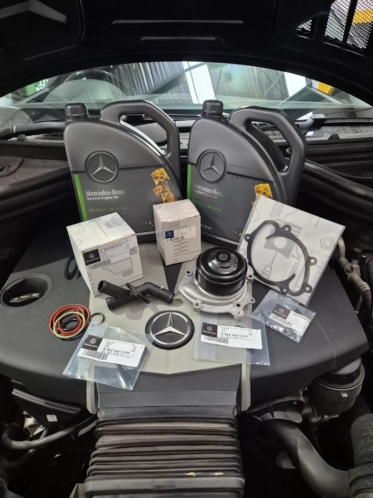 Mercedes-Benz engine components and genuine oil, including a water pump, gaskets, and seals, arranged on a vehicle engin