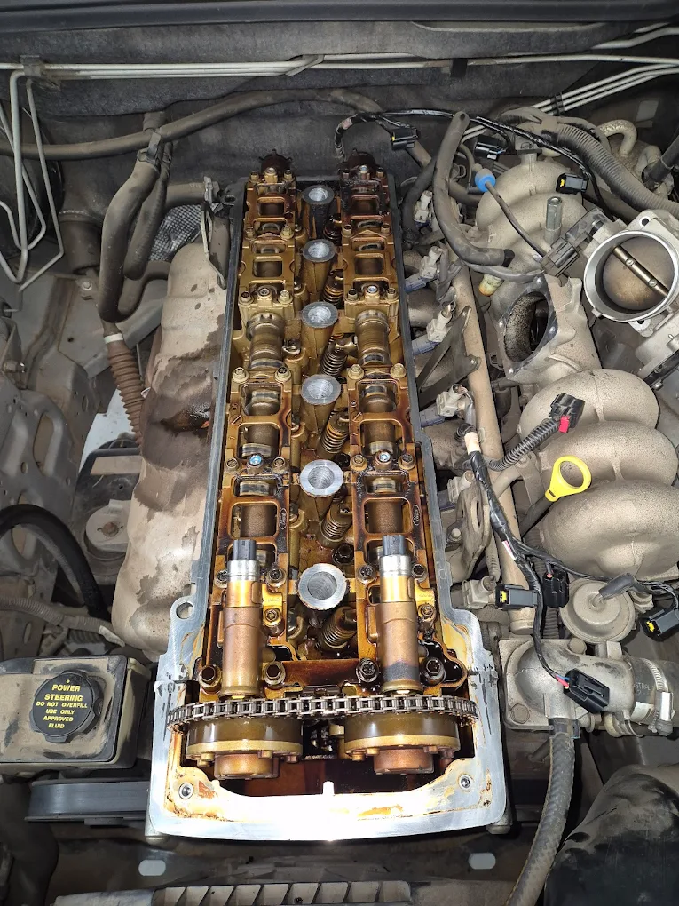 Mercedes-Benz engine components with exposed valve cover, showing camshafts and timing chain