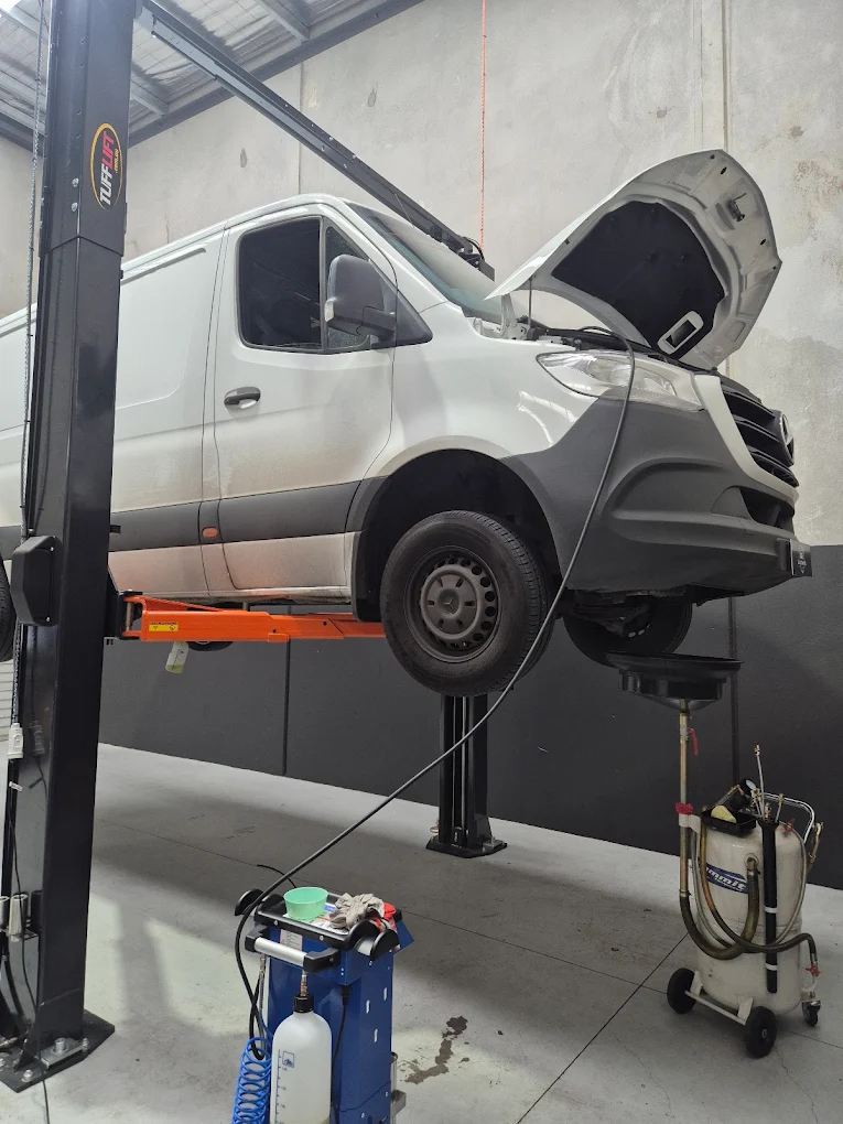 Mercedes-Benz van on a hydraulic lift in a workshop, hood raised for engine inspection